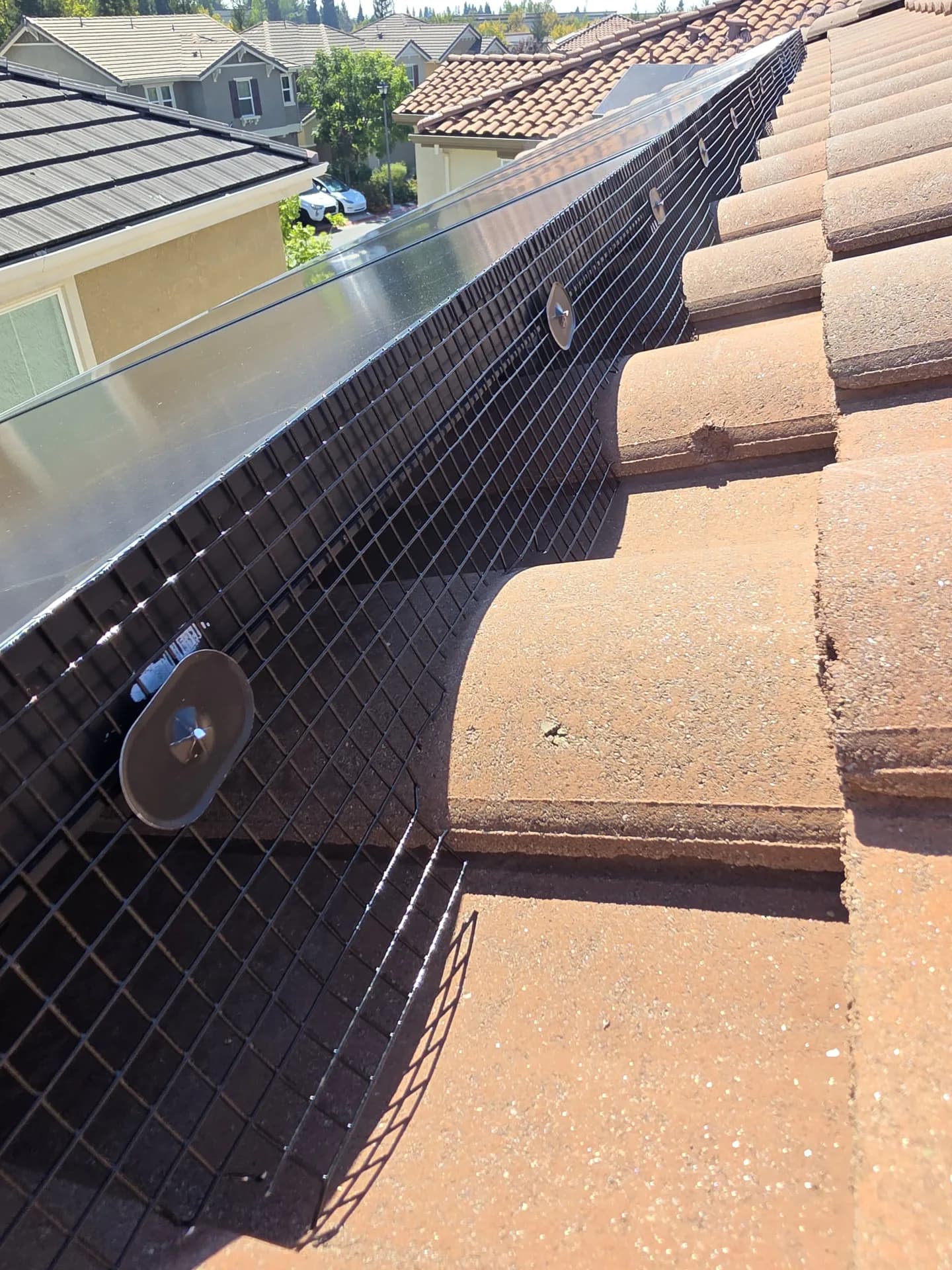 Wire mesh birdproofing installed between solar panels and clay roof tiles