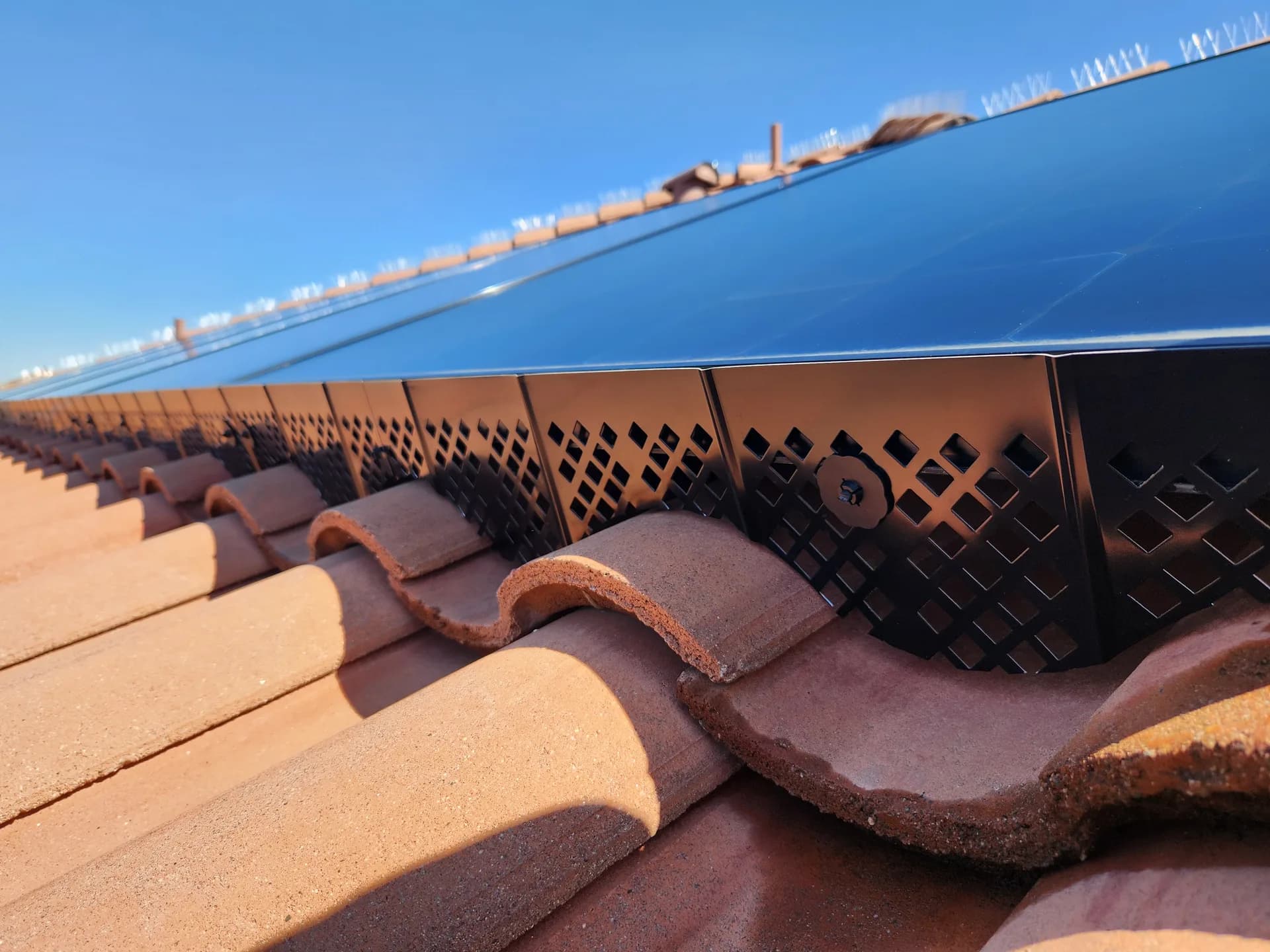 Close-up of solar bird screen closing the gap under panels on a tile roof