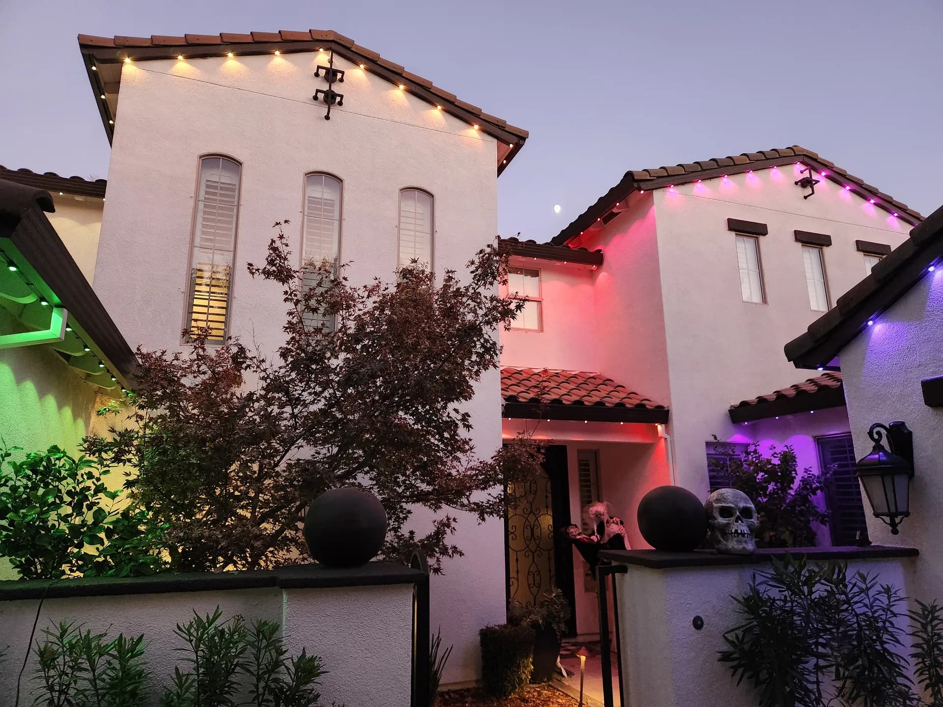 Permanent LED holiday lights in Halloween colors on a stucco home at dusk