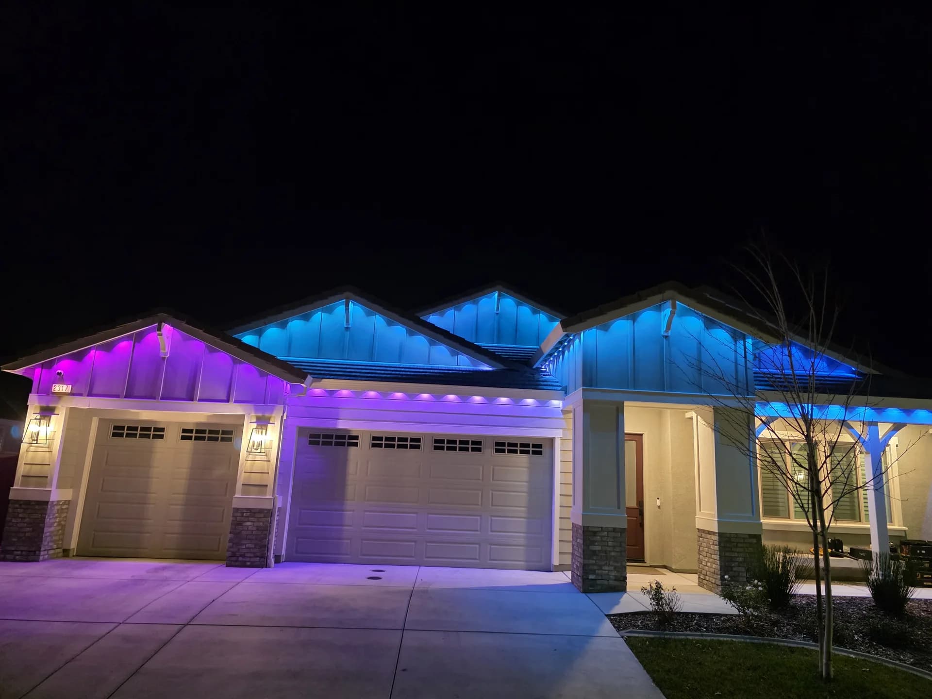 Color-changing permanent Christmas lights in purple and blue on a ranch-style home