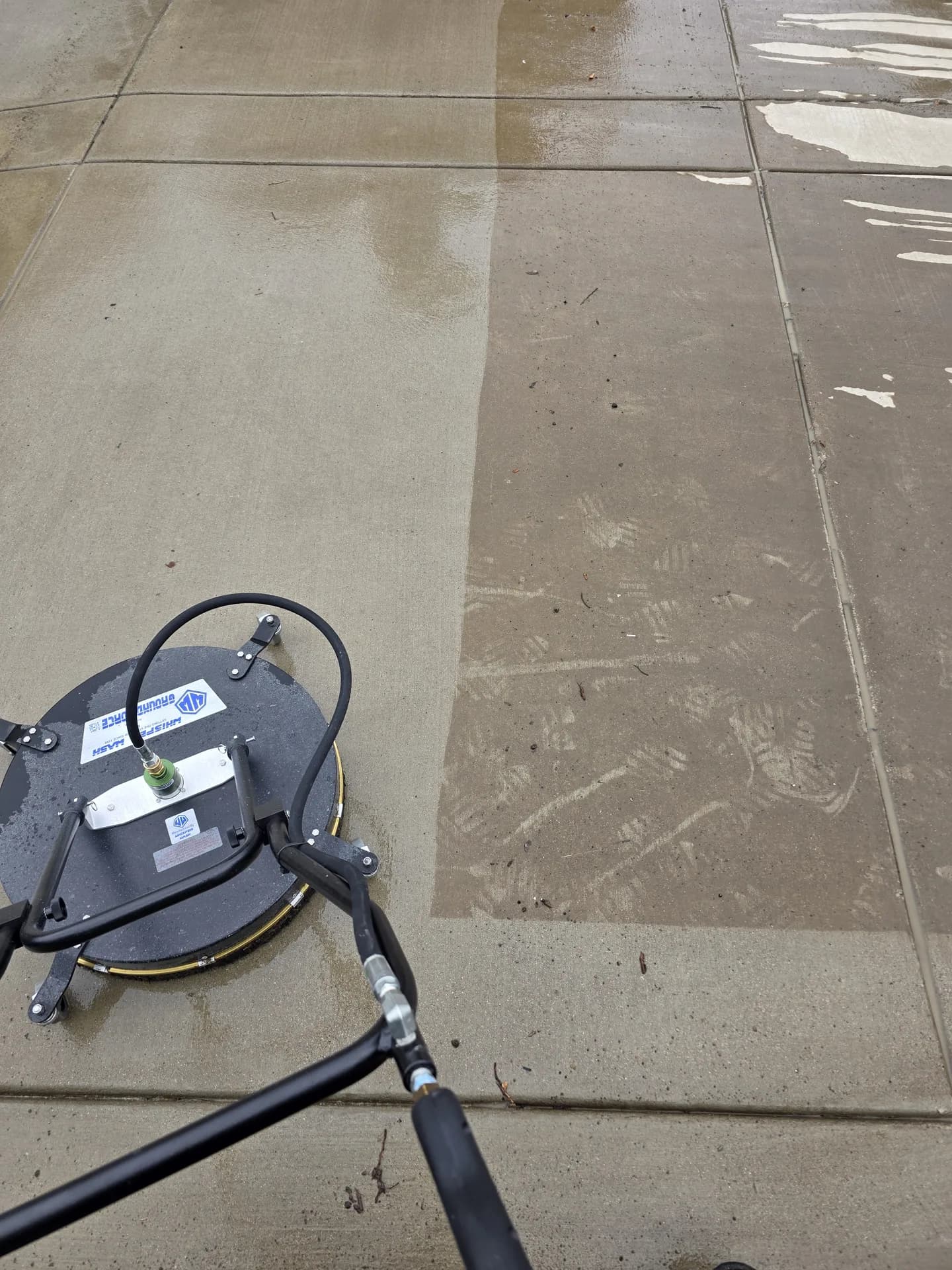Driveway pressure washing in progress with a surface cleaner on scored concrete